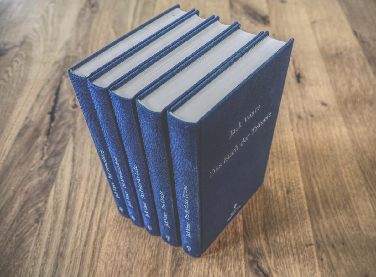 Fünf blaue Hardcover-Bücher liegen ordentlich in einer Reihe, mit dem Rücken nach links, auf einer Holzoberfläche.