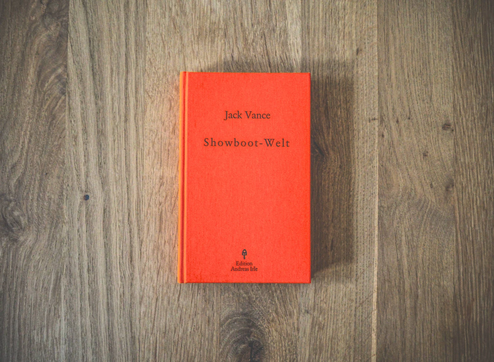 Auf einer Holzfläche liegt ein rotes Hardcover-Buch mit dem Titel „Showboot-Welt“ von Jack Vance.