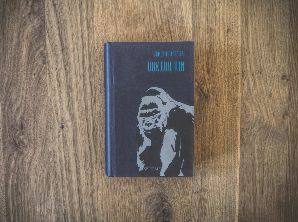 Cover von „Doktor Ain“ von James Tiptree Jr., das einen stilisierten Gorilla auf einer Holzoberfläche zeigt.