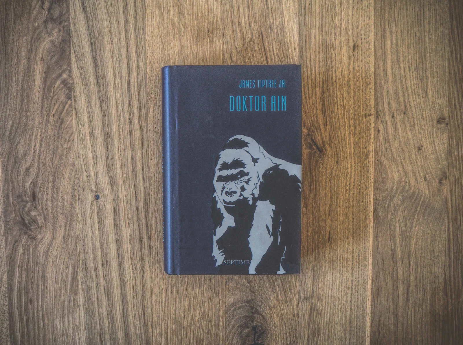 Cover von „Doktor Ain“ von James Tiptree Jr., das einen stilisierten Gorilla auf einer Holzoberfläche zeigt.