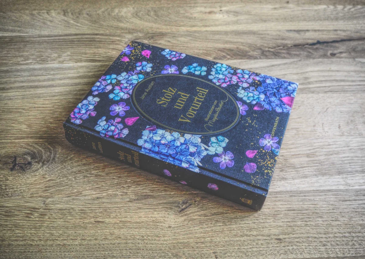 Gebundenes Buch mit dem Titel „Stolz und Vorurteil“ mit floral gemustertem Cover, auf Holzuntergrund platziert.