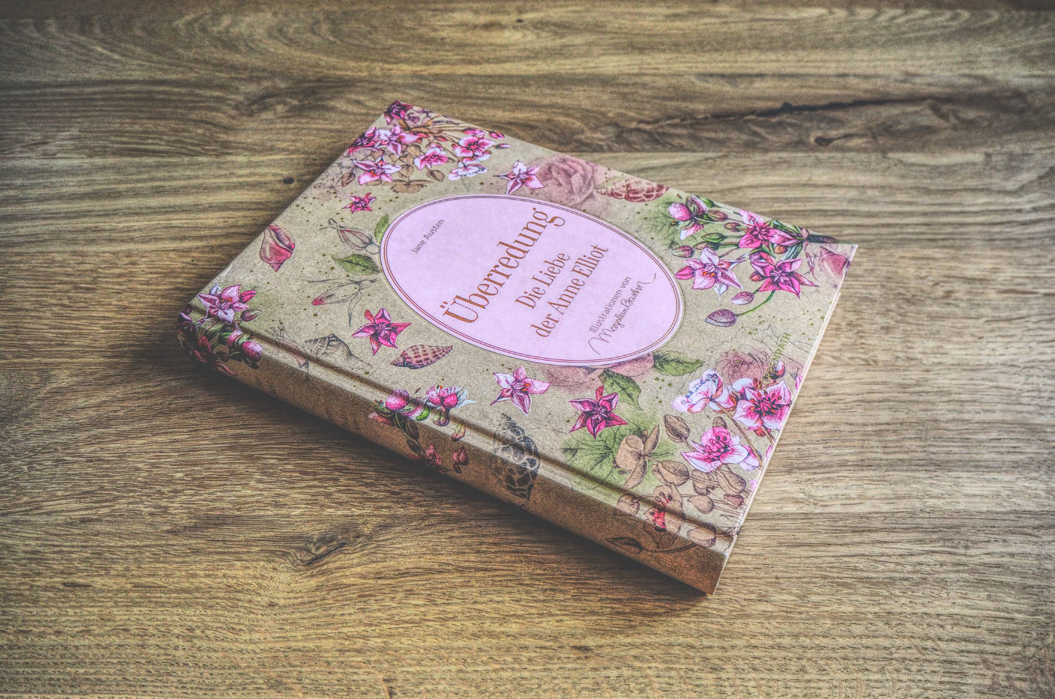Ein Buch mit rosa Blumen auf einem Holztisch.