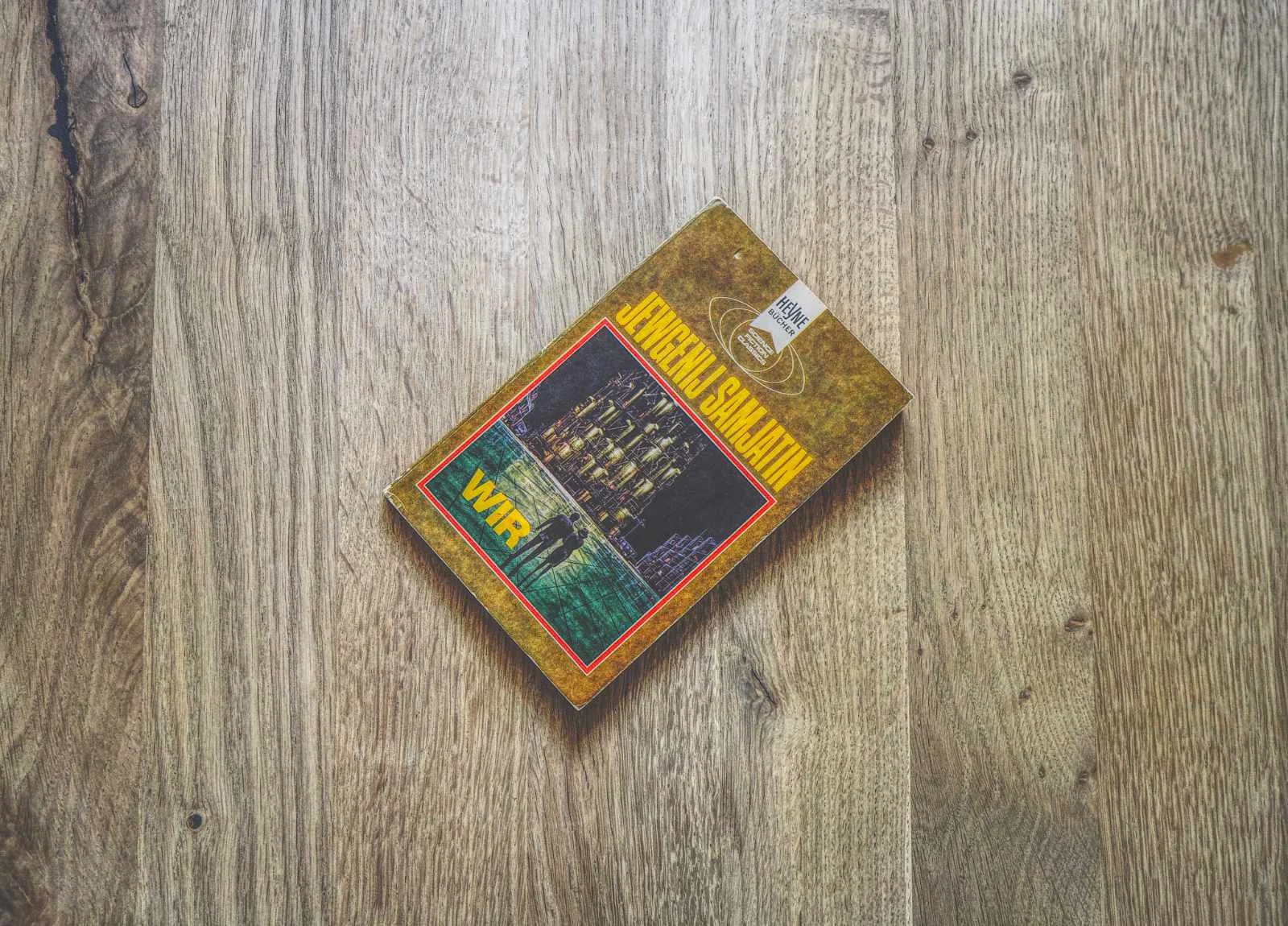 Ein Taschenbuch mit dem Titel "Wir" von Jewgenij Samjatin liegt auf einer Holzfläche.