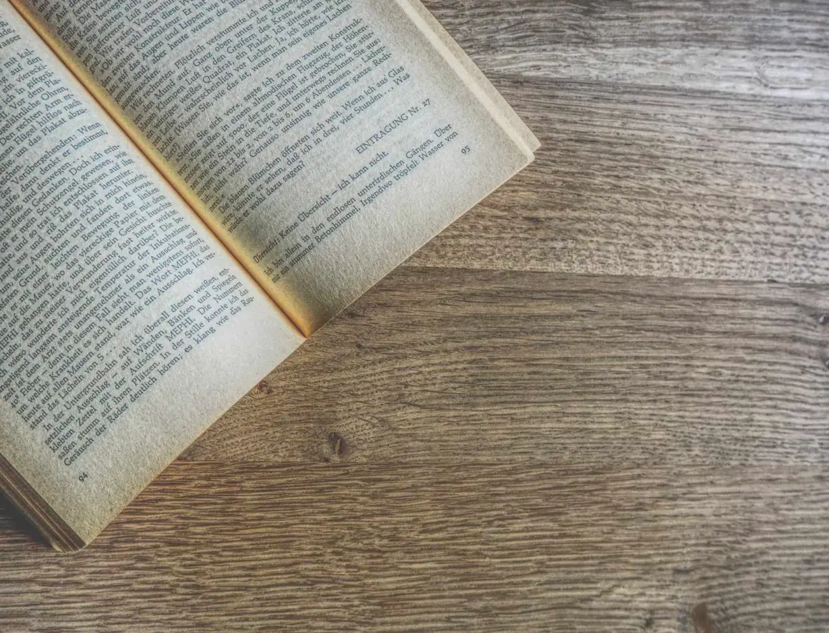 Ein aufgeschlagenes Buch liegt auf einer hölzernen Oberfläche und zeigt gedruckten Text auf vergilbten Seiten.