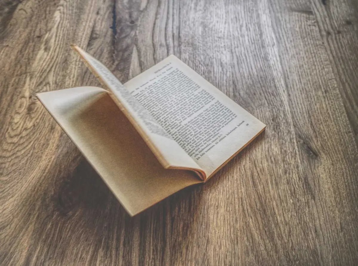 Ein aufgeschlagenes Buch mit gealterten Seiten liegt auf einer hölzernen Unterlage, wobei eine Seite teilweise umgeschlagen ist.