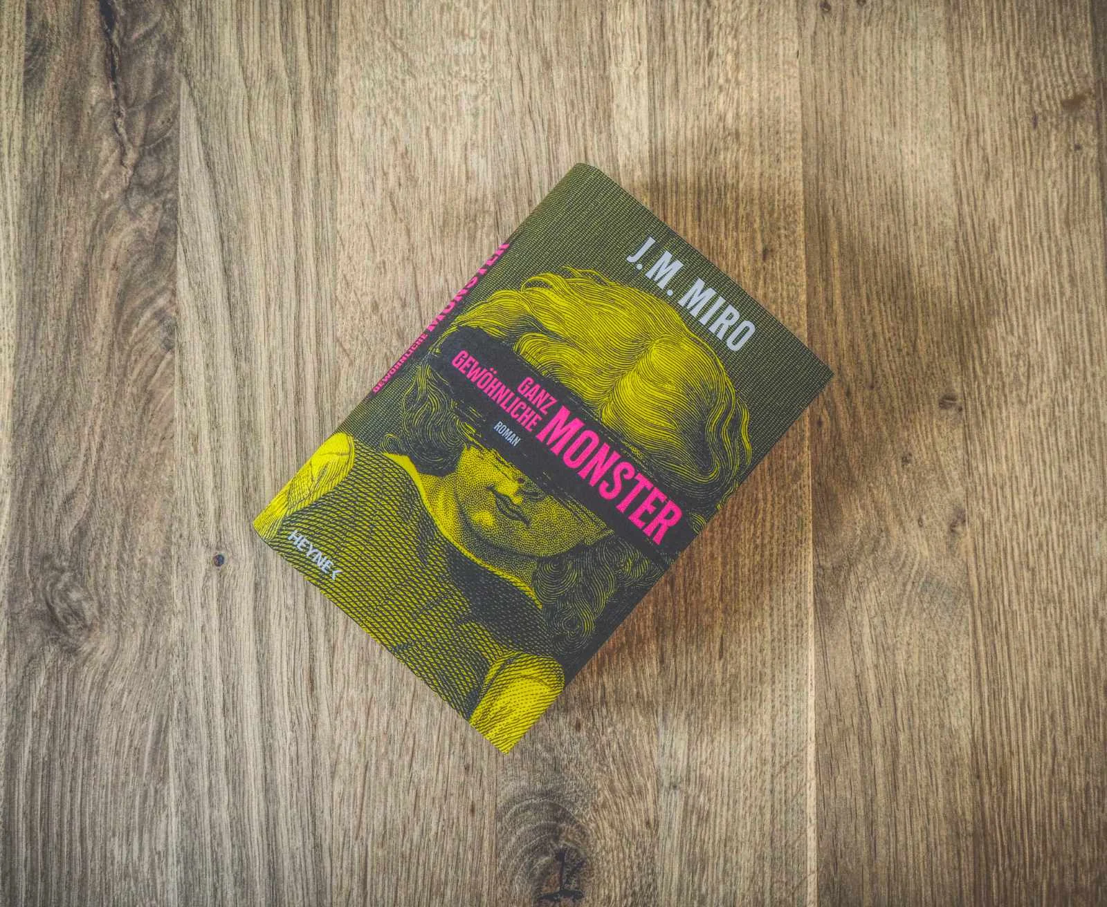 Auf einer Holzfläche liegt ein Buch mit dem Titel „Ganz gewöhnliche Monster“ von J.M. Miro. Auf dem Cover sind in gedeckten Farben ein Kind und ein Vogel abgebildet.