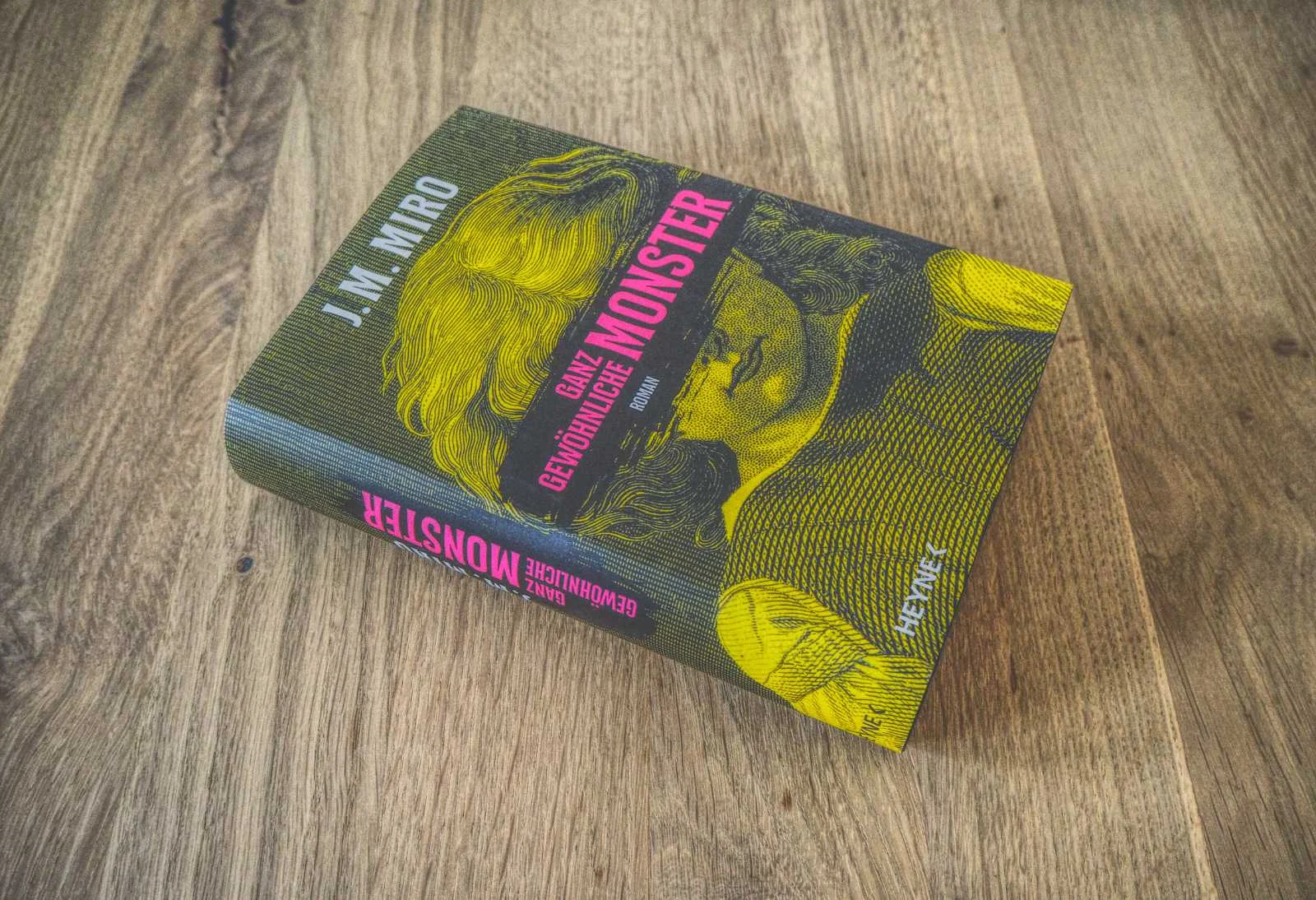 Auf einer Holzoberfläche liegt ein Buch mit dem Titel „Ganz gewöhnliche Monster“ von J.M. Miro. Auf dem Cover ist ein gelb-schwarzes Bild mit einem Gesicht zu sehen.