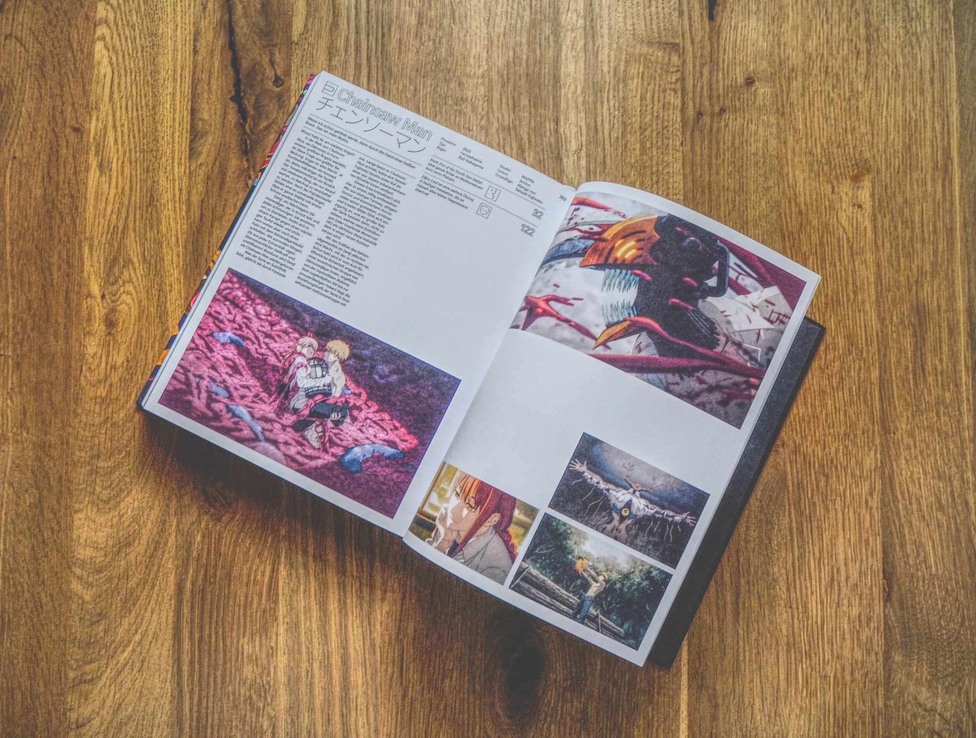 Ein aufgeschlagenes Magazin auf einem Holztisch zeigt Seiten mit japanischem Text und mehreren bunten Anime-Bildern.