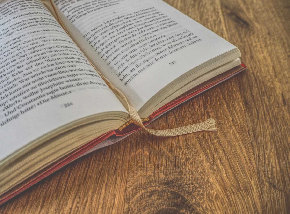 Ein offenes Buch mit einem beigen Lesezeichenband auf einem Holztisch.