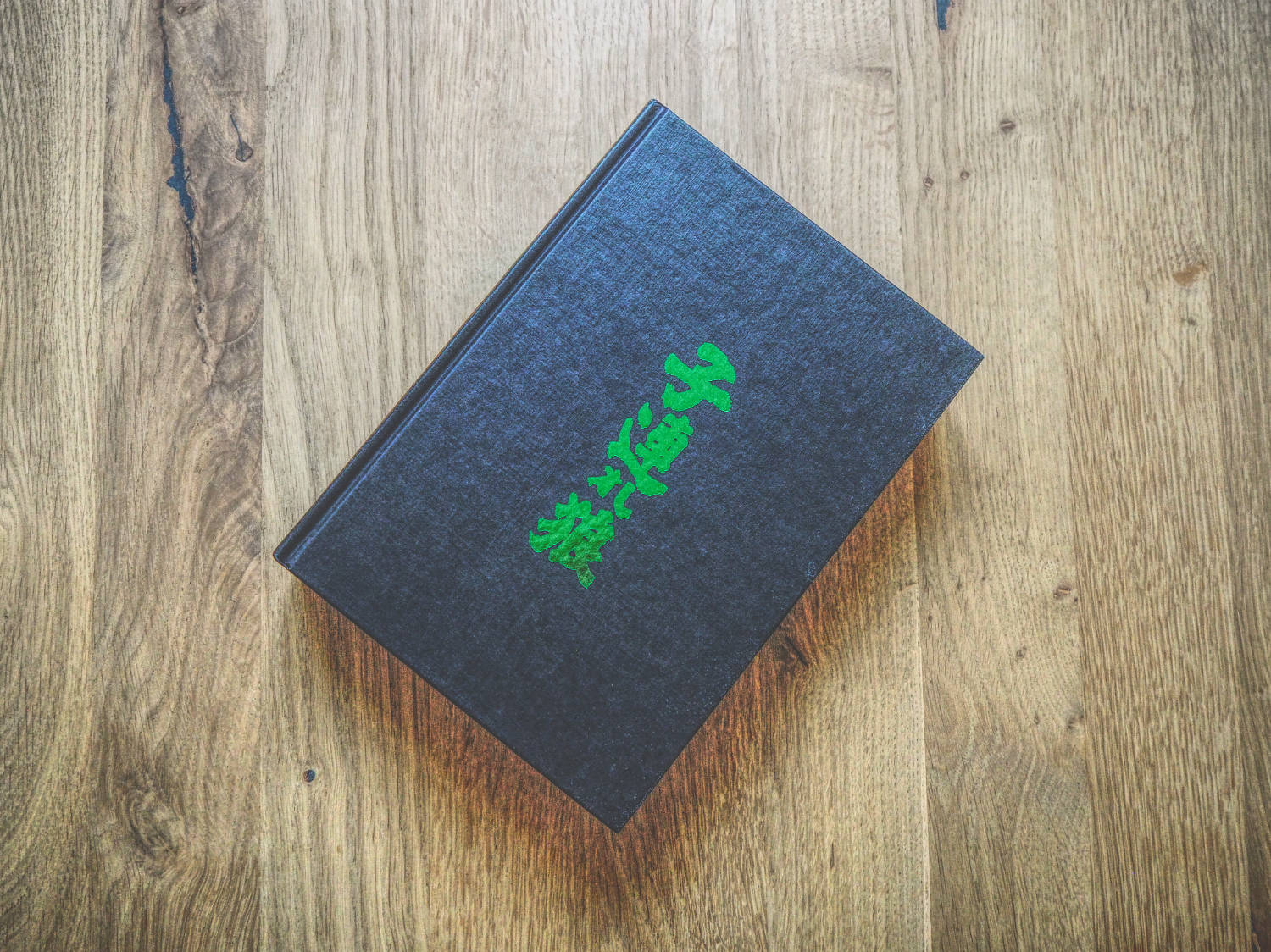 Ein schwarzes Buch mit grüner Schrift darauf auf einem Holztisch.