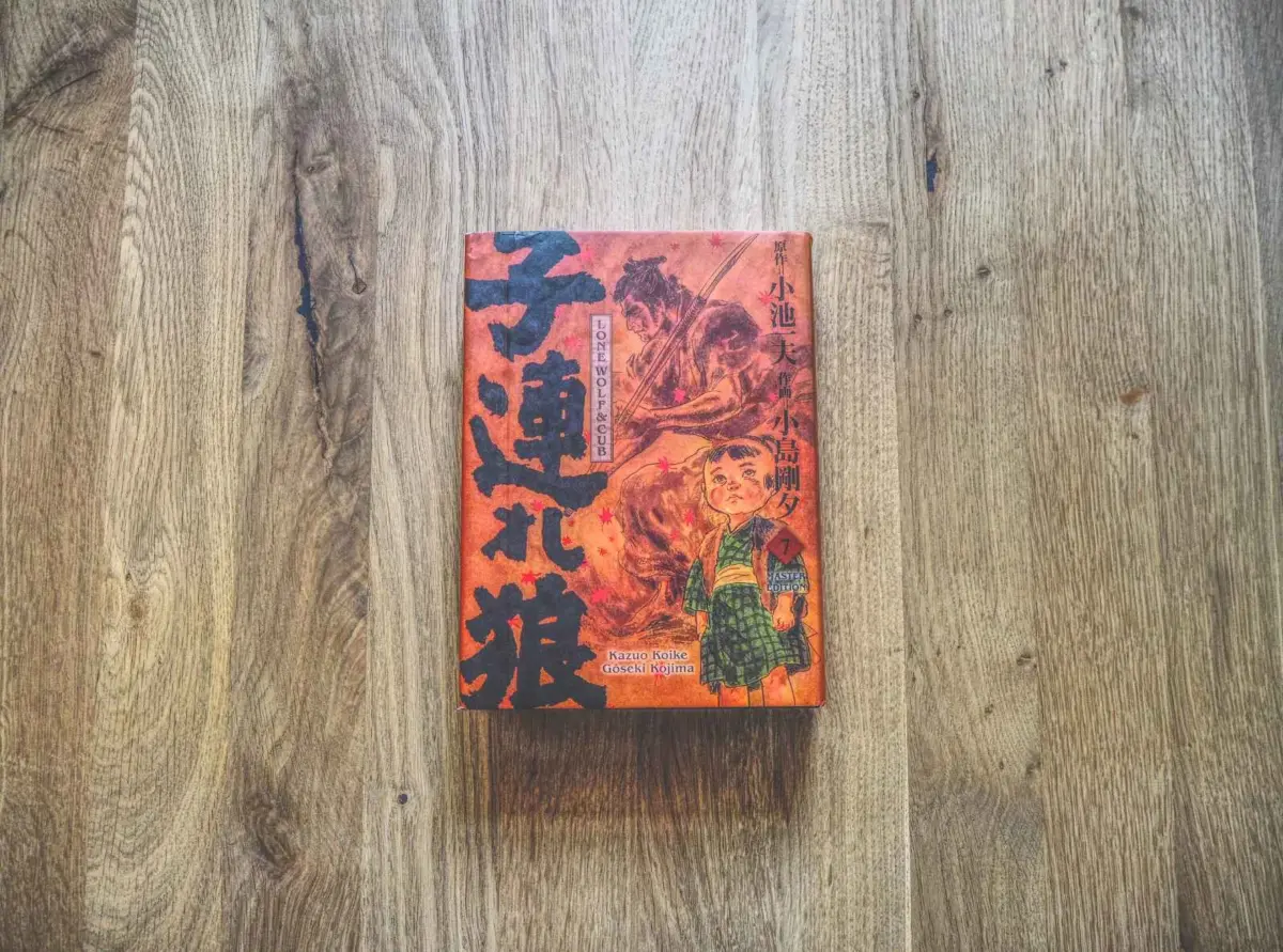 Ein japanisches Buch mit einem illustrierten Einband, auf dem ein Kind und ein Wolf abgebildet sind, liegt auf einer Holzfläche.