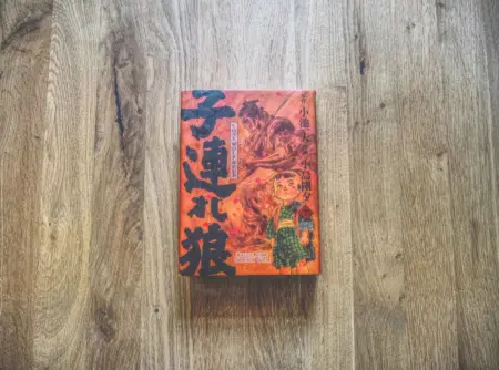 Ein japanisches Buch mit einem illustrierten Einband, auf dem ein Kind und ein Wolf abgebildet sind, liegt auf einer Holzfläche.