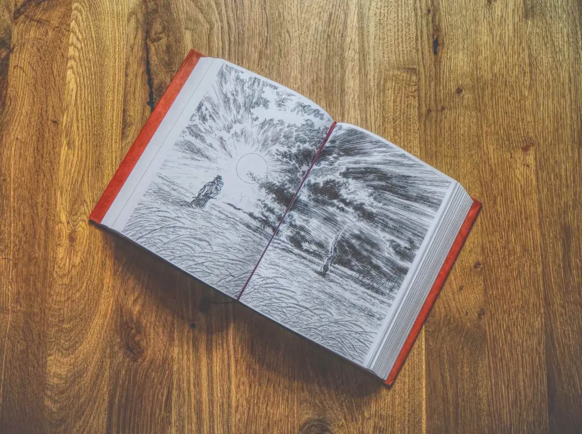 Ein aufgeschlagenes Buch mit schwarz-weißen Landschaftsillustrationen auf den Seiten, das auf einer Holzunterlage liegt.