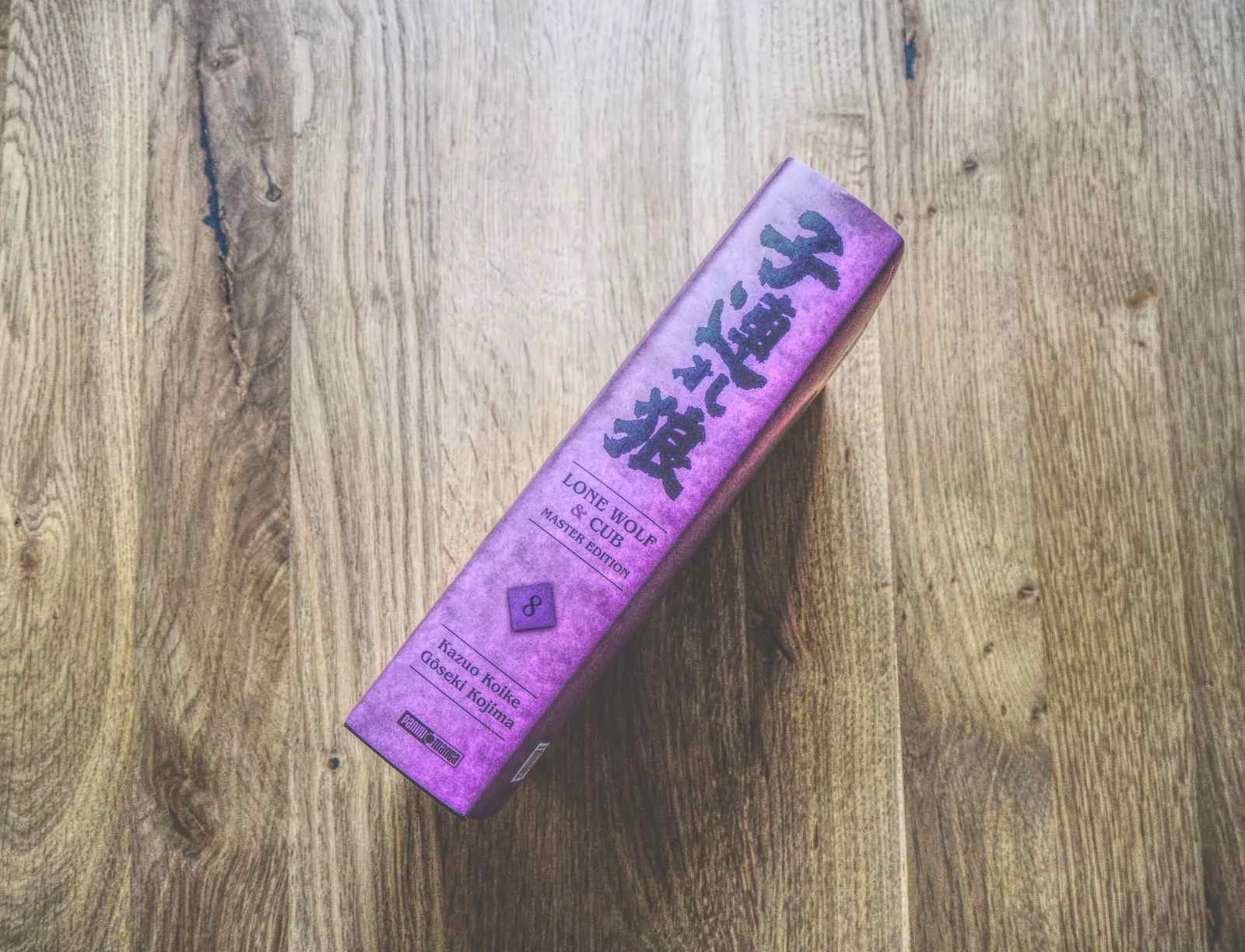 Ein gebundenes Buch mit dem Titel "Lone Wolf and Cub, 8" mit japanischen Schriftzeichen auf dem Buchrücken wird auf eine Holzfläche gelegt.