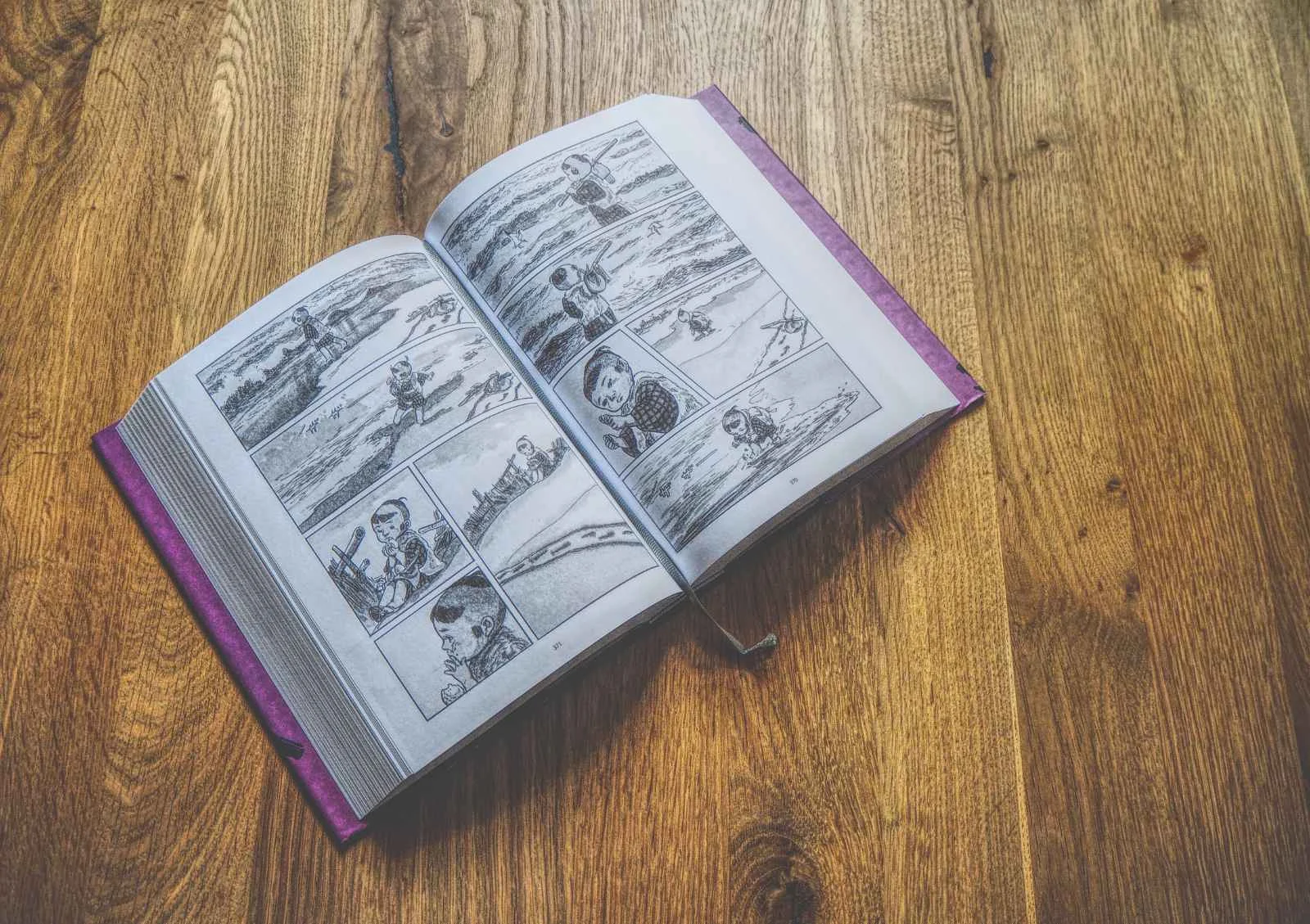 Eine aufgeschlagene illustrierte Graphic Novel mit schwarz-weißen Comic-Panels auf einer Holzoberfläche.