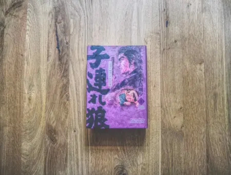 Ein japanisches Buch mit lilafarbenem Einband und illustrierten Schriftzeichen liegt auf einer Holzfläche.