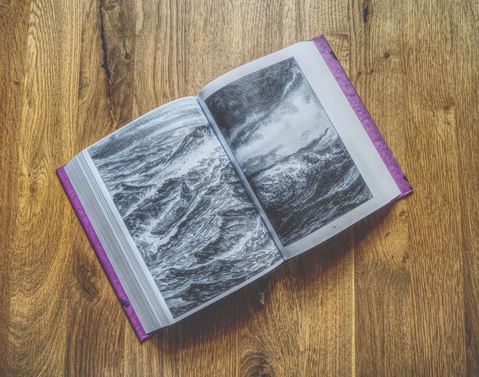 Ein aufgeschlagenes Buch mit Schwarz-Weiß-Bildern von rauen Meereswellen, die auf einer Holzoberfläche liegen.