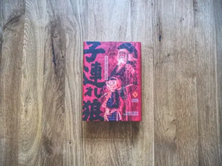 Ein japanisches Buch mit rotem Einband, auf dem zwei Schriftzeichen abgebildet sind, liegt auf einer Holzfläche.