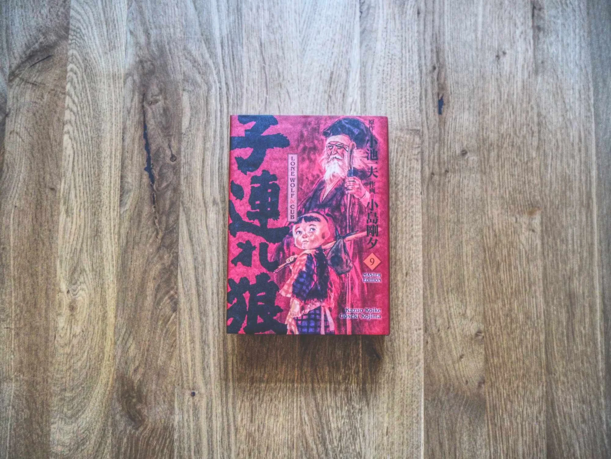 Ein japanisches Buch mit rotem Einband, auf dem zwei Schriftzeichen abgebildet sind, liegt auf einer Holzfläche.