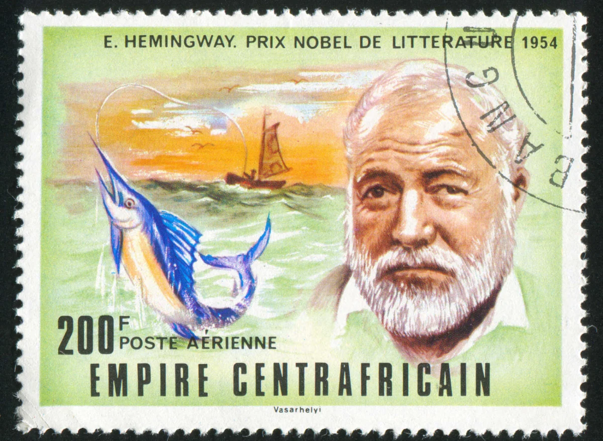 Eine Briefmarke mit einem Porträt von Ernest Hemingway, einem Segelfisch und einem Boot auf dem Wasser. Der Text lautet „E. Hemingway, Prix Nobel de Littérature 1954“ und der Briefmarkenwert beträgt 200F von Empire Centrafricain.