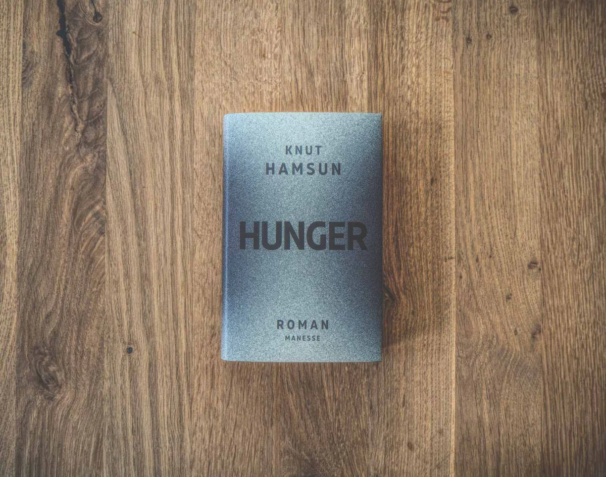 Auf einer Holzfläche liegt ein Buch mit dem Titel „Hunger“ von Knut Hamsun. Der Einband ist grau mit schwarzem Text.