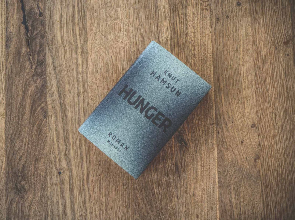 Auf einer Holzfläche liegt ein Buch mit dem Titel „Hunger“ von Knut Hamsun.