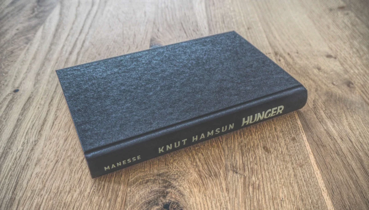 Ein gebundenes Buch mit dem Titel „Hunger“ von Knut Hamsun liegt geschlossen auf einer Holzfläche.