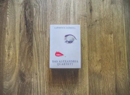 Auf einer hölzernen Unterlage liegt eine Box mit "Das Alexandria Quartett" von Lawrence Durrell; das Cover zeigt ein Auge und ein Paar rote Lippen.