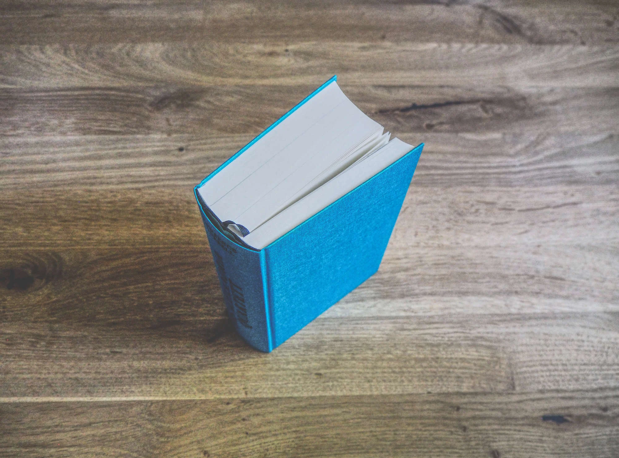 Ein geschlossenes, gebundenes Buch mit blauem Einband wird aufrecht auf eine Holzunterlage gestellt.