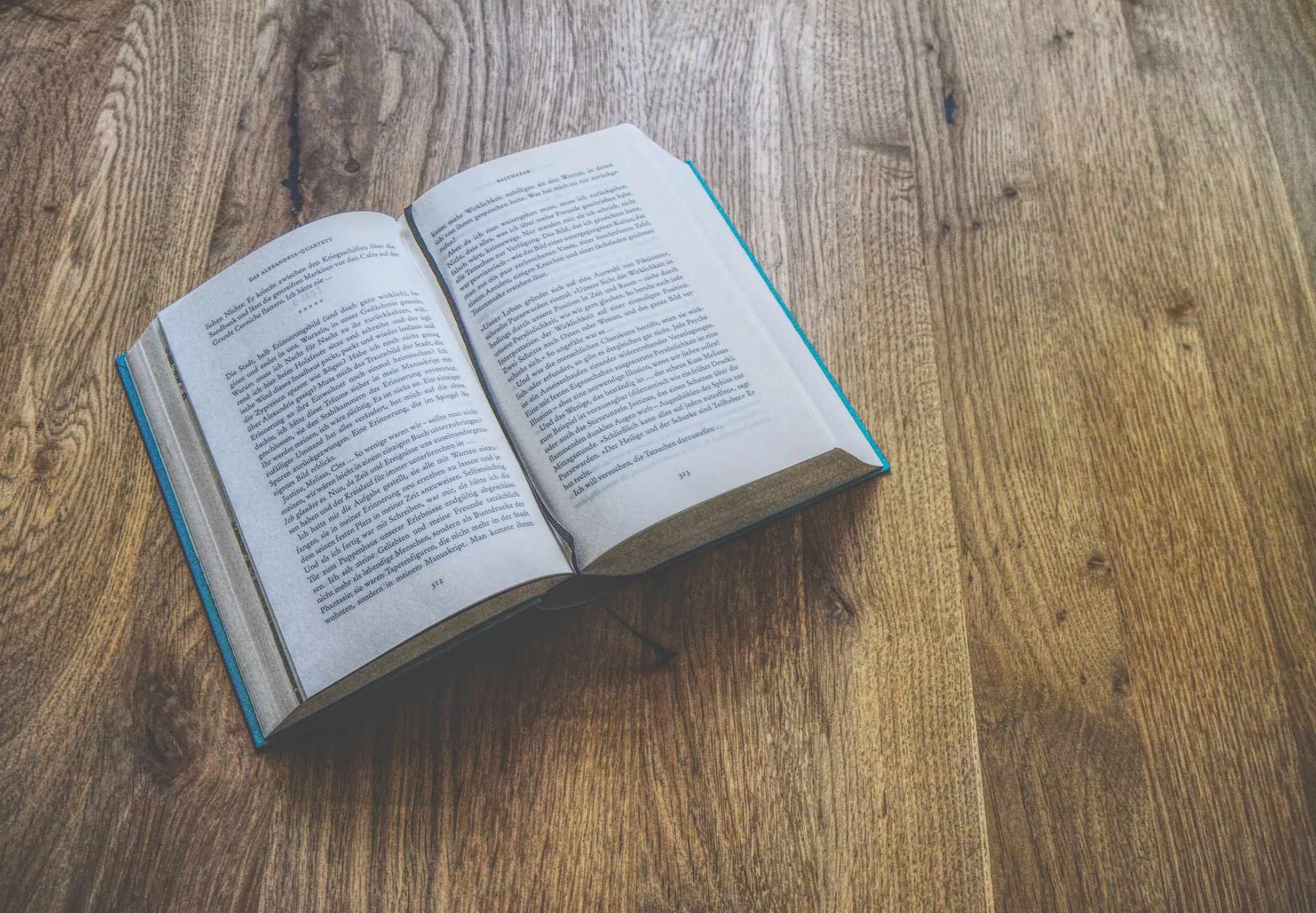 Auf einem Holztisch liegt ein aufgeschlagenes Buch, das zwei Seiten Text enthält.