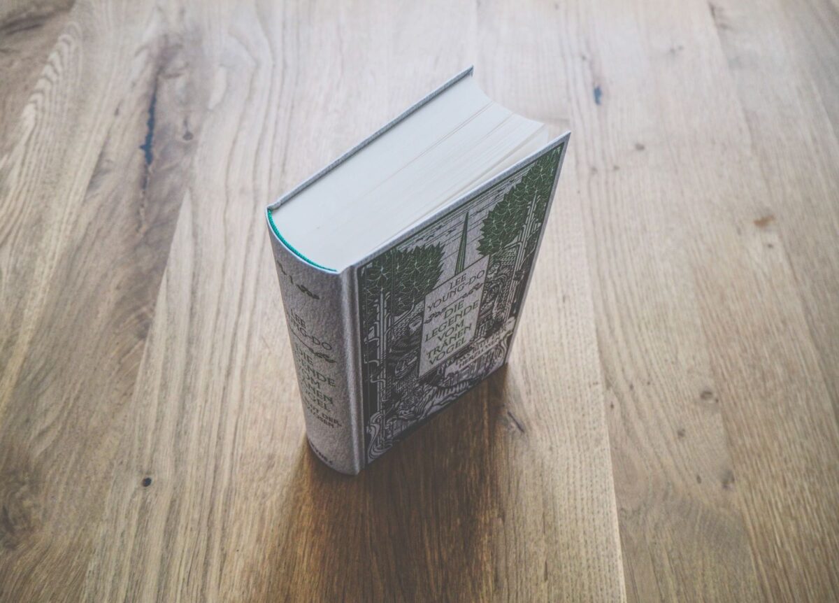 Ein gebundenes Buch steht aufrecht auf einer Holzoberfläche und zeigt seinen Buchrücken mit komplizierten grün-weißen Mustern.