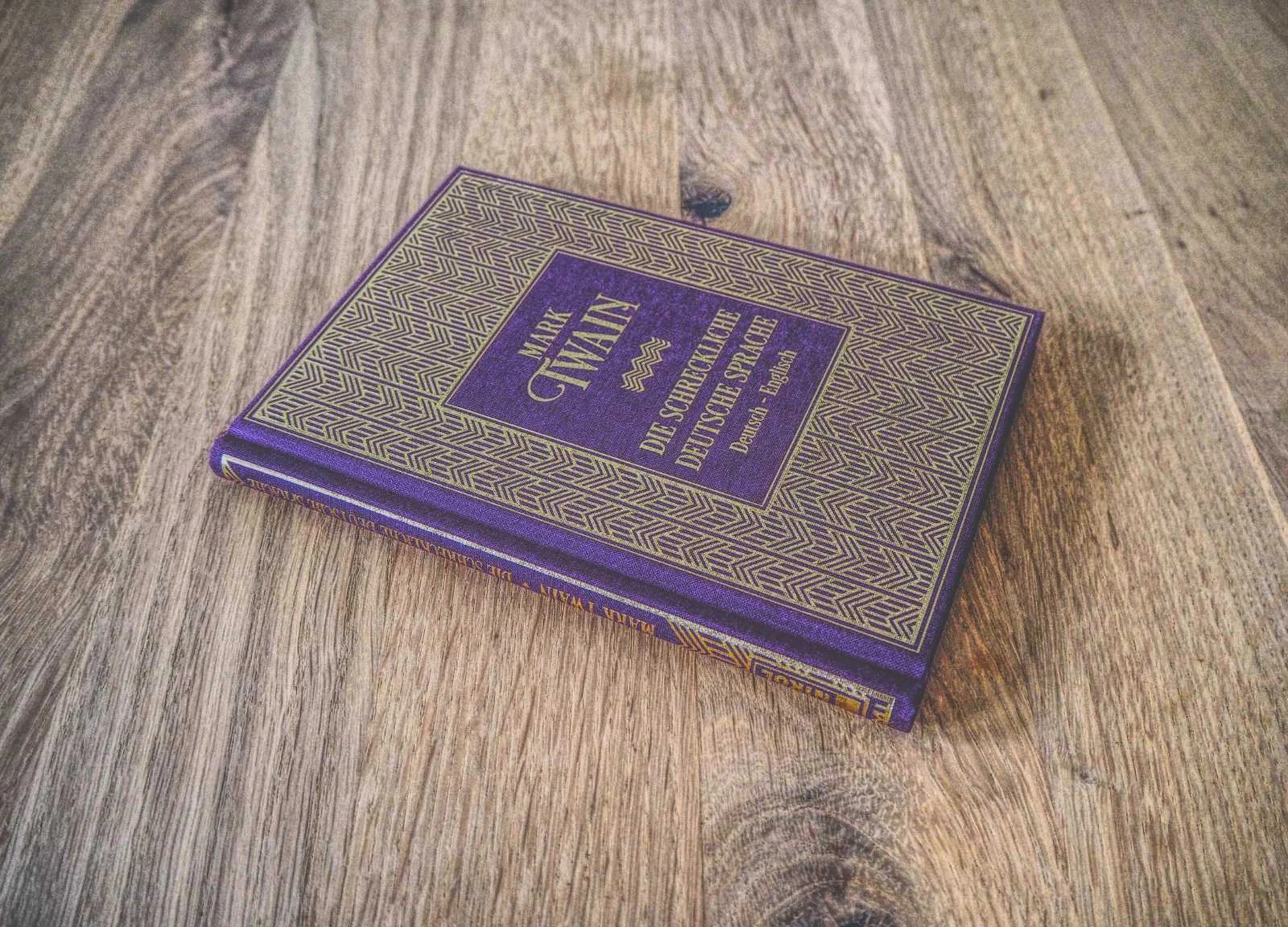 Auf einer Holzfläche liegt ein gebundenes Buch mit dem deutschen Titel „Die schreckliche deutsche Sprache“ von Mark Twain.