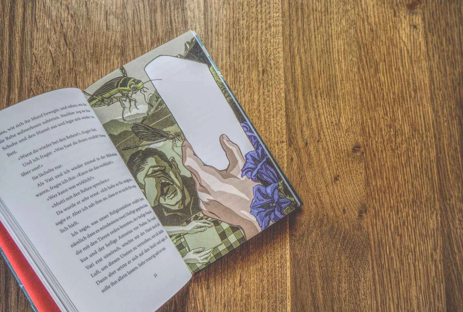 Ein aufgeschlagenes Buch mit Text auf der linken Seite und einem illustrierten Bild auf der rechten Seite, das eine Hand und Blumen zeigt, mit einem weißen Lesezeichen im Inneren. Das Buch ruht auf einer Holzunterlage.
