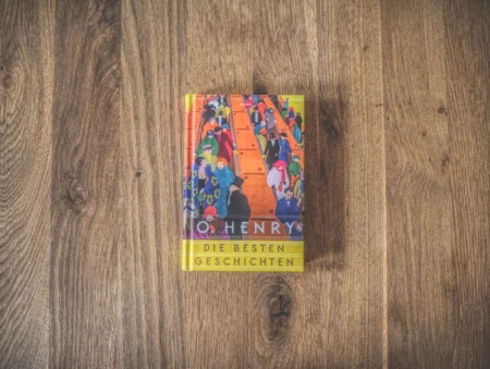 Ein Buch mit dem Titel „Die besten Geschichten“ von O. Henry auf einer Holzoberfläche. Das Cover zeigt eine Illustration von Menschen in leuchtenden Farben.