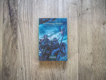 Ein deutsches Buch mit dem Titel „Der traurige Henker“ von Fritz Leiber mit einem illustrierten Cover, auf dem zwei gepanzerte, mit Waffen ausgestattete Figuren vor einem hölzernen Hintergrund abgebildet sind.