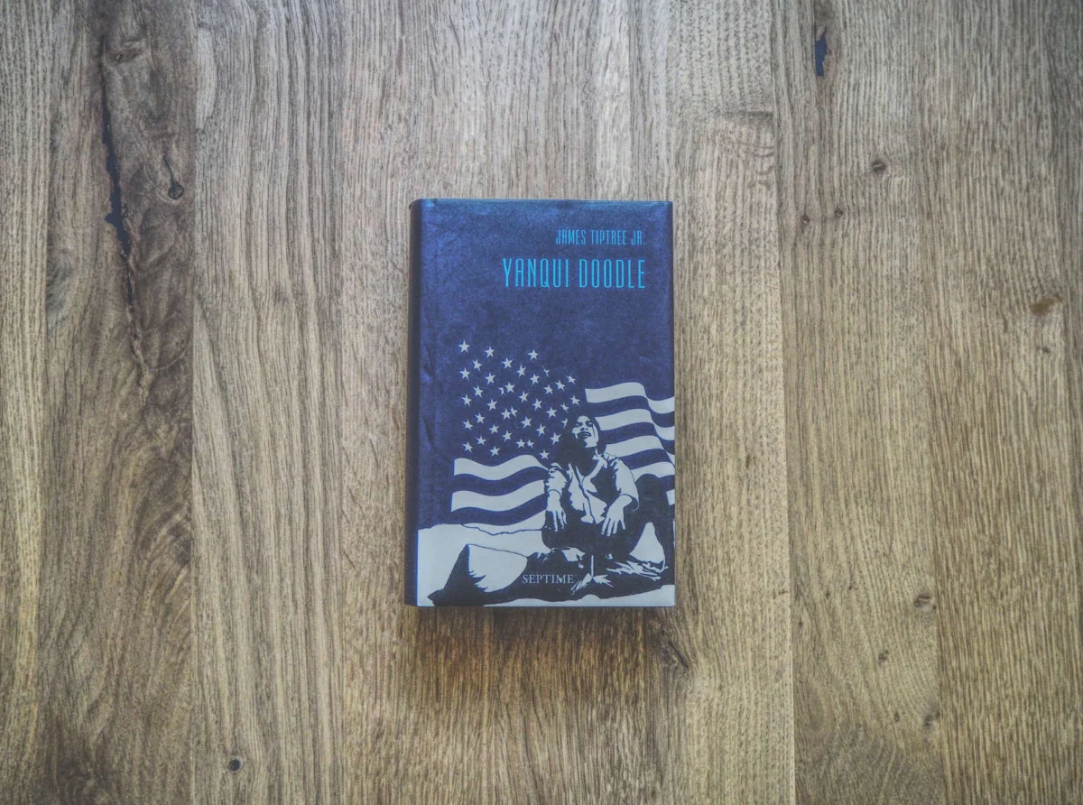 Auf einer Holzoberfläche liegt ein Buch mit dem Titel „Yanqui Doodle“ und auf dem Cover ist ein Mann abgebildet, der unter einer amerikanischen Flagge sitzt.