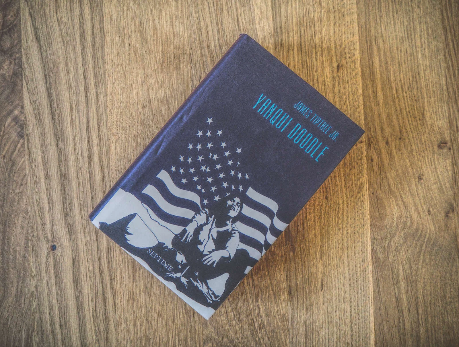 Ein Buch mit dem Titel „Yanqui Doodle“ von James Tiptree Jr. liegt auf einer Holzoberfläche. Auf dem Cover ist ein sitzender Mann vor dem Hintergrund einer amerikanischen Flagge abgebildet.