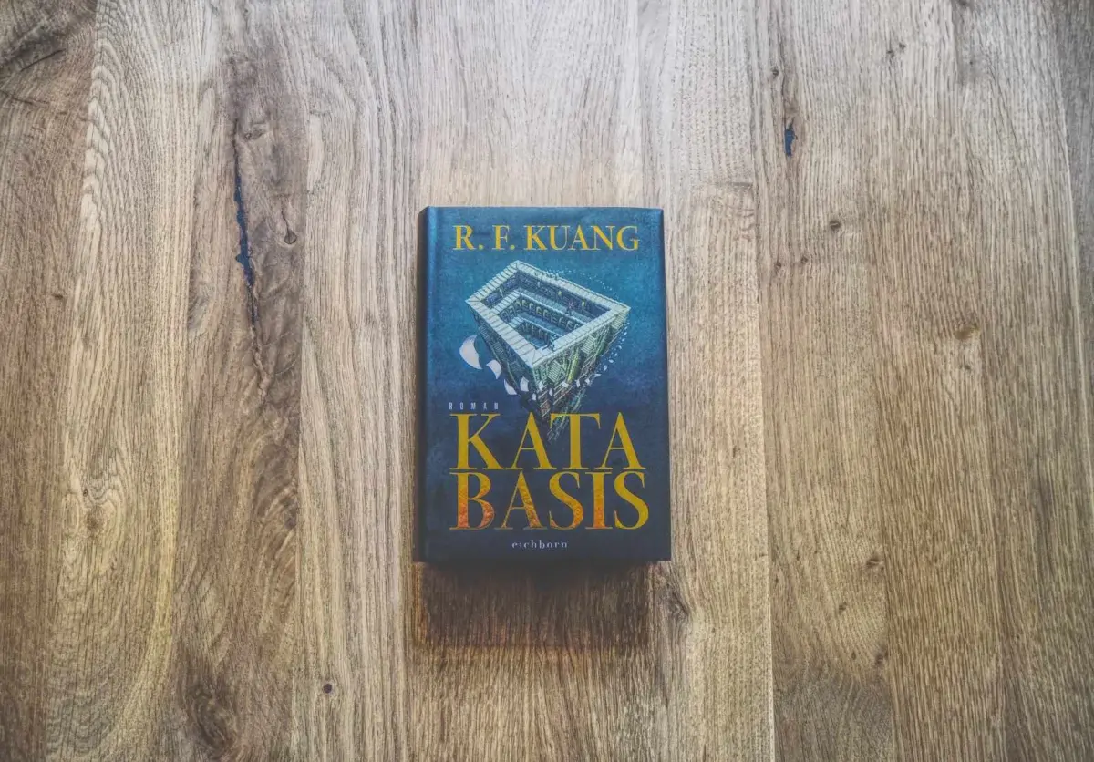 Ein gebundenes Buch mit dem Titel "KATABASIS" von R. F. Kuang liegt auf einer Holzfläche.