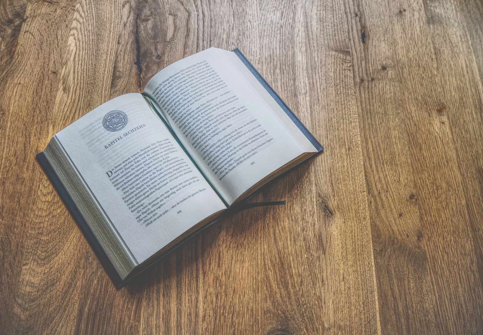 Ein aufgeschlagenes Buch liegt auf einer hölzernen Oberfläche und zeigt Text auf den beiden sichtbaren Seiten.