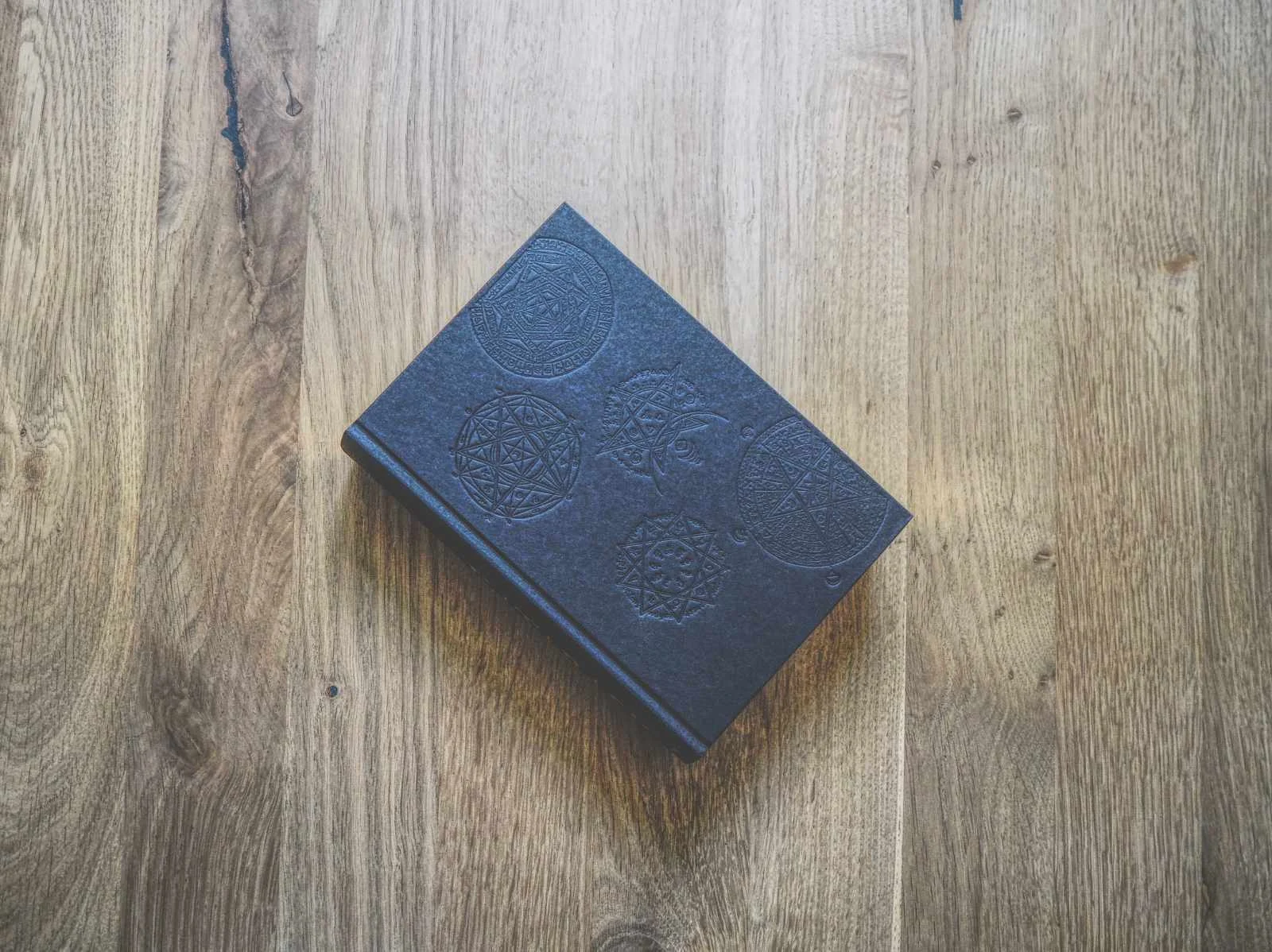 Ein geschlossenes, schwarzes, geprägtes Notizbuch mit geometrischen Mustern liegt auf einer Holzoberfläche.