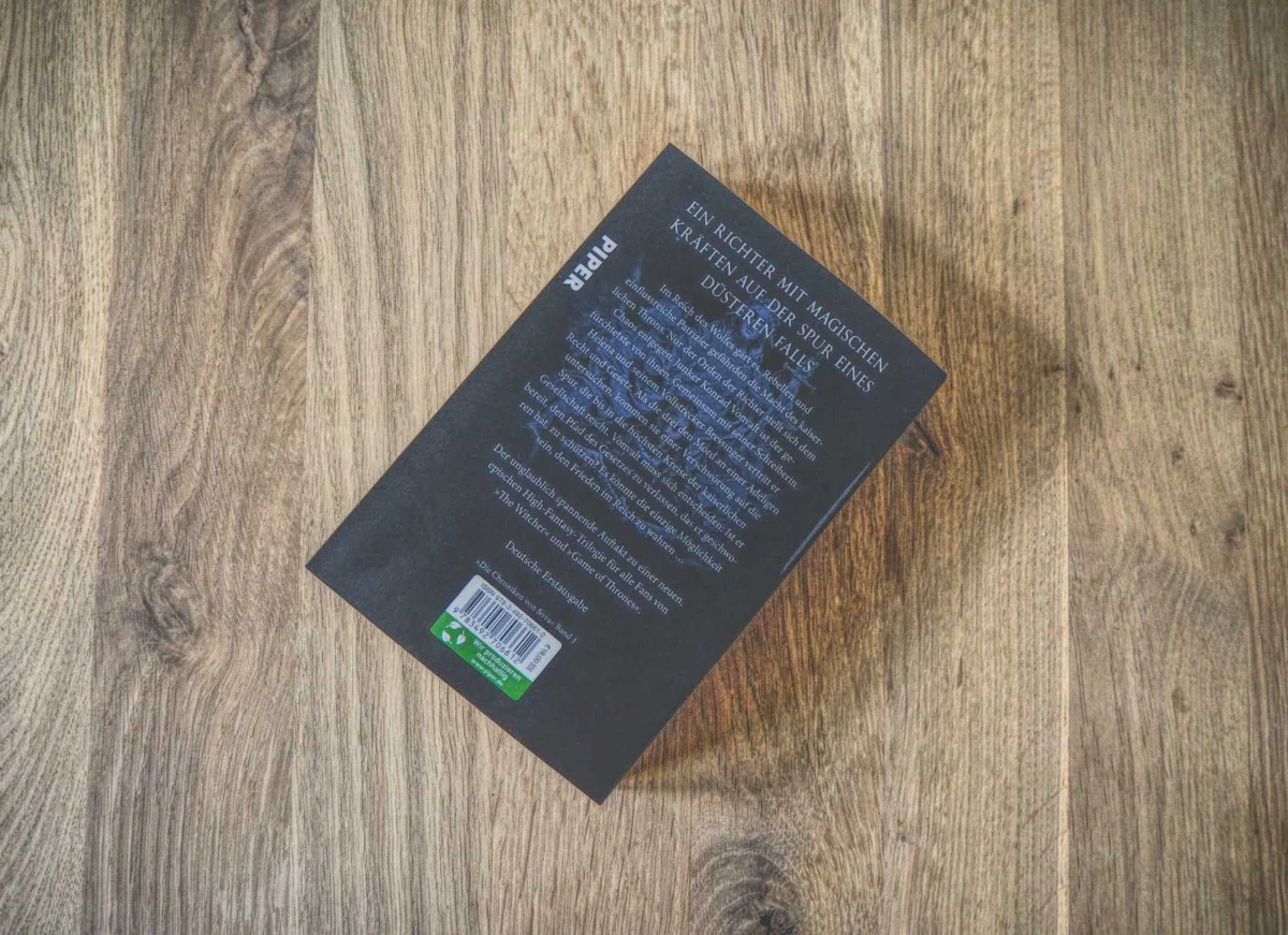 Auf einer Holzoberfläche liegt ein schwarzes Buch mit deutschem Text auf der Rückseite. In der unteren linken Ecke ist ein Barcode sichtbar.