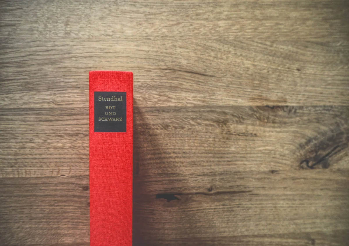 Ein rotes Hardcover-Buch mit der Aufschrift „Stendhal - Rot und Schwarz“ steht aufrecht auf einer Holzoberfläche.