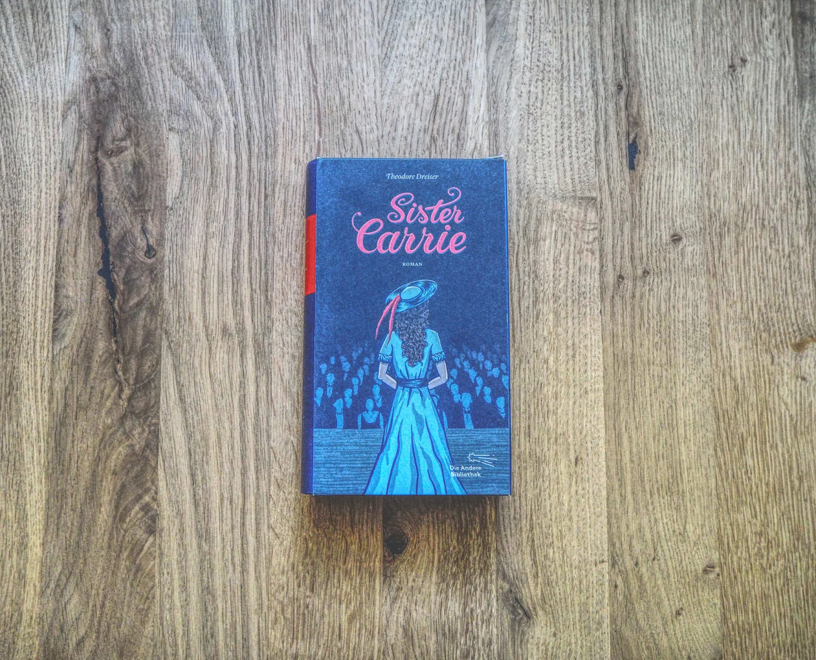 Ein Buch mit dem Titel „Sister Carrie“ von Theodore Dreiser mit einer Coverillustration einer Dame in einem blauen Kleid und Hut, die auf einer Holzoberfläche steht.