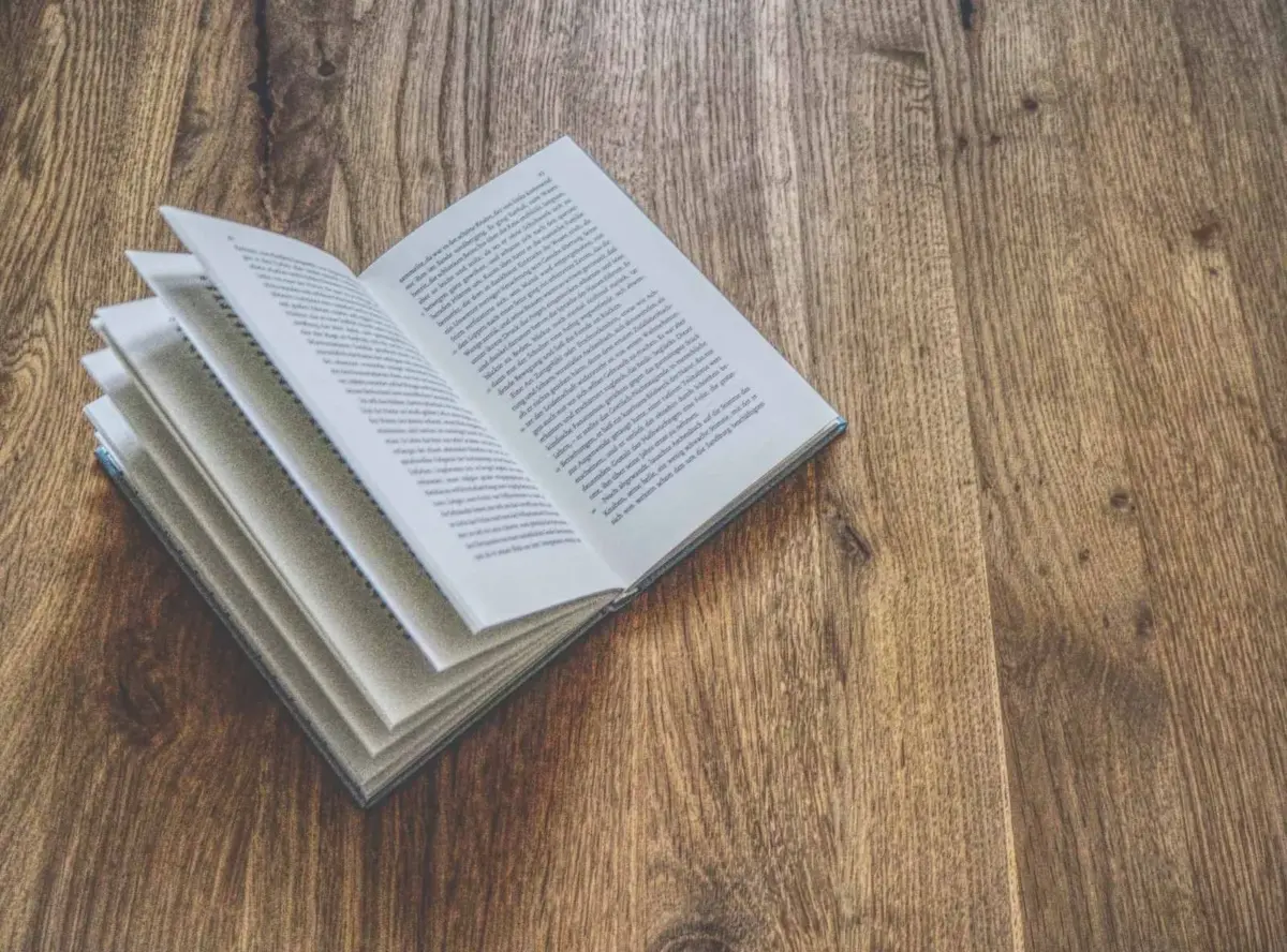 Auf einer Holzoberfläche liegt ein offenes Buch, die Seiten sind leicht gespreizt.