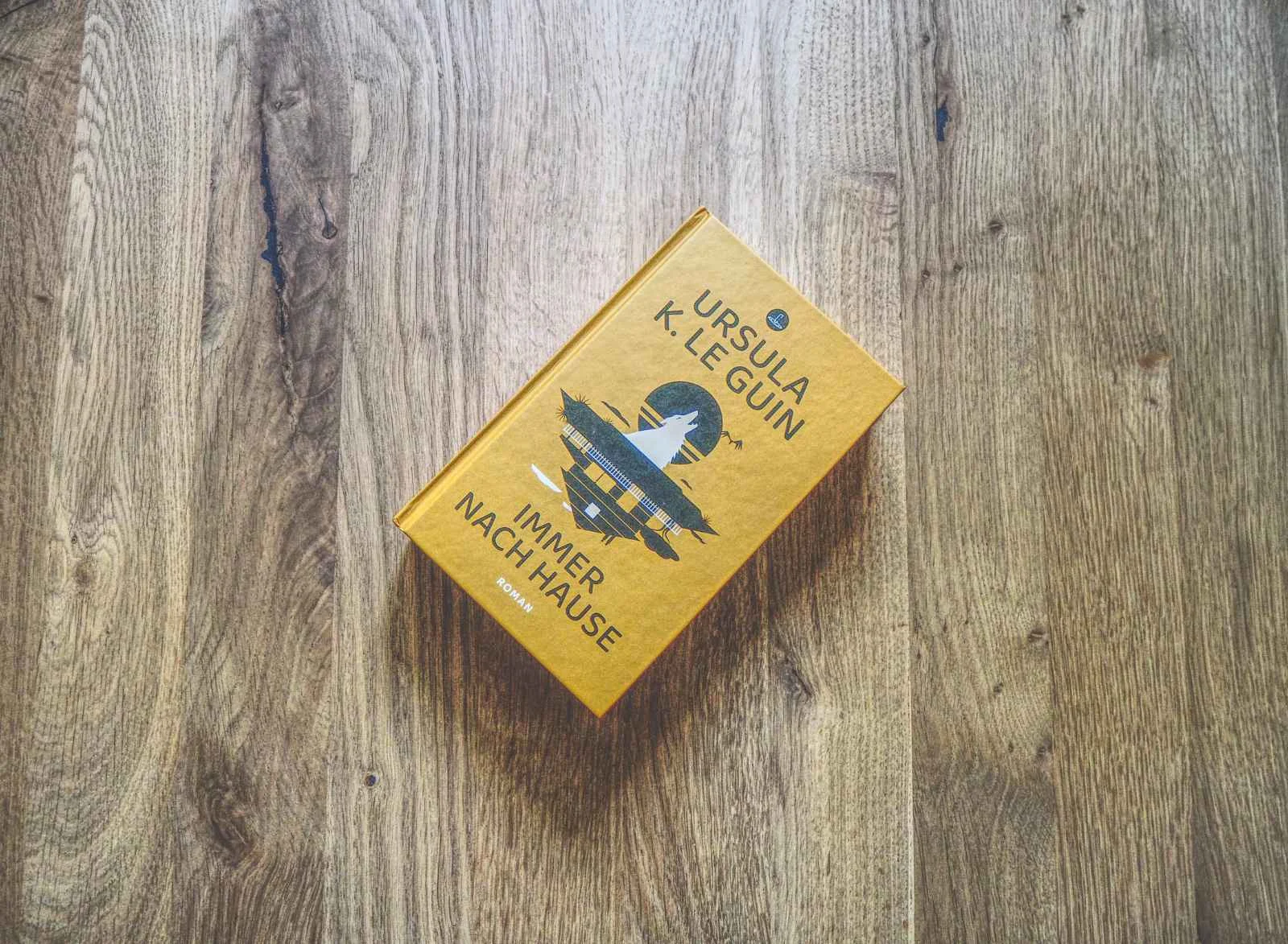 Ein gelbes, gebundenes Buch mit dem Titel "Immer nach Hause" von Ursula K. Le Guin liegt auf einer Holzfläche.