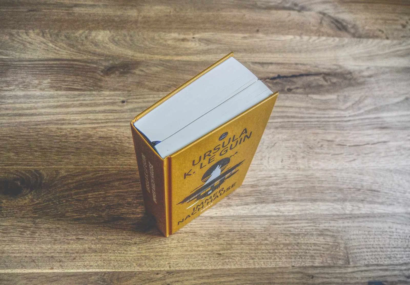 Ein gebundenes Buch mit dem Titel "Ursula K. Le Guin" liegt geschlossen auf einer hölzernen Unterlage, schräg von oben betrachtet.