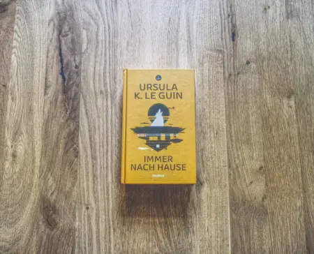 Ein gebundenes Buch mit dem Titel "Immer nach Hause" von Ursula K. Le Guin liegt auf einer Holzfläche.