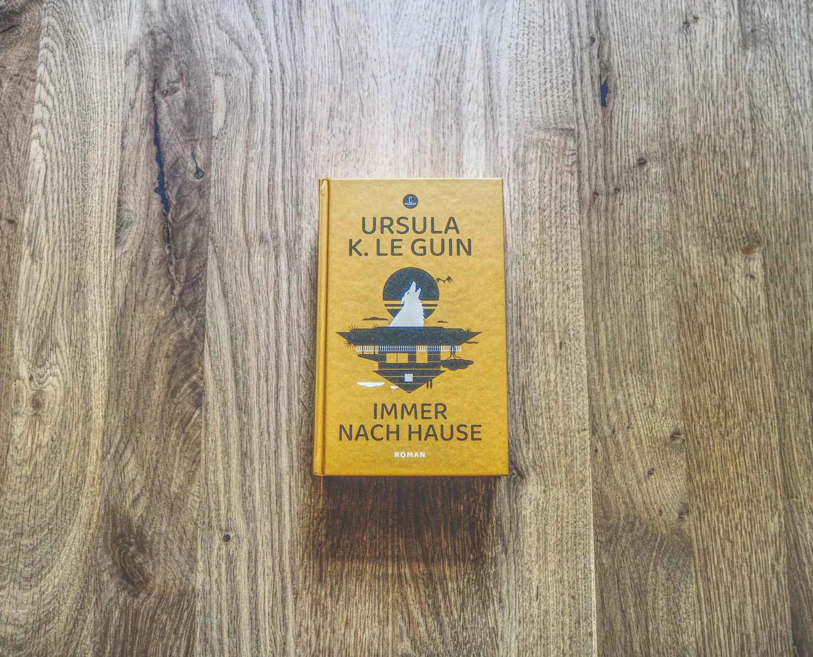 Ein gebundenes Buch mit dem Titel "Immer nach Hause" von Ursula K. Le Guin liegt auf einer Holzfläche.