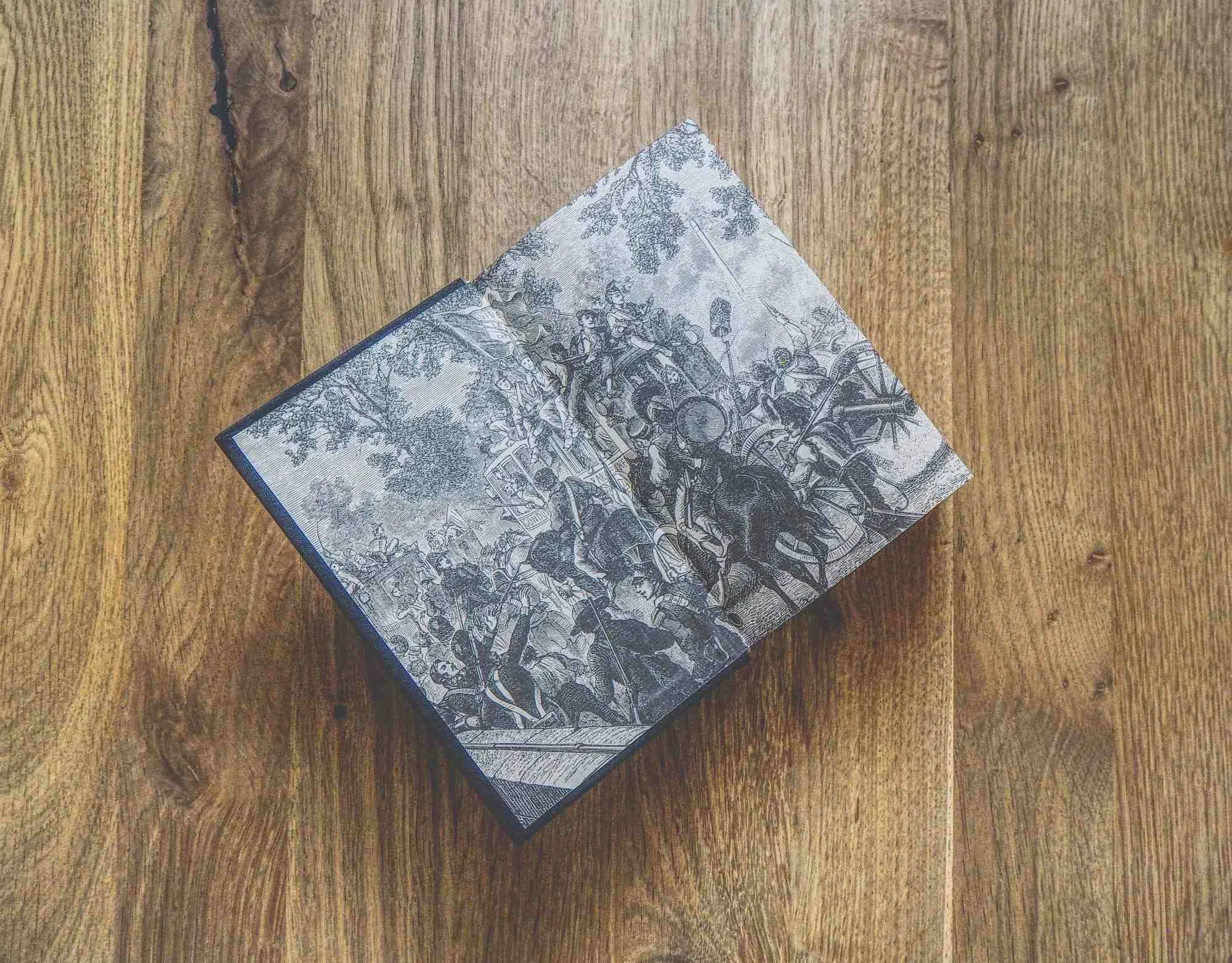 Ein aufgeschlagenes Buch mit einer historischen Schwarz-Weiß-Illustration, das auf einer Holzunterlage liegt.