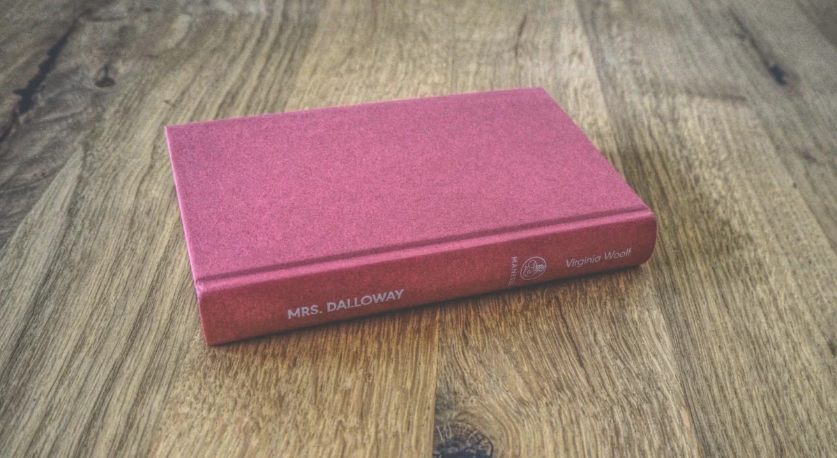 Auf einer Holzfläche liegt ein rotes gebundenes Buch mit dem Titel „Mrs. Dalloway“ von Virginia Woolf.